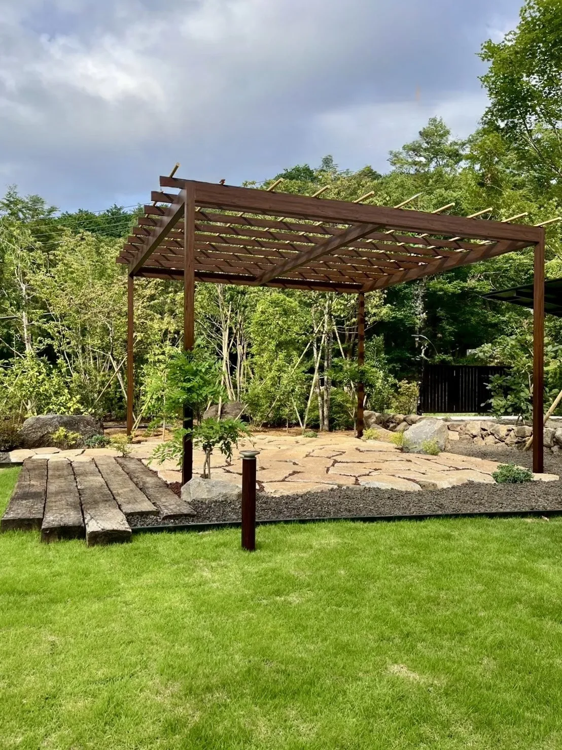木製パーゴラと石張りのテラスが映える、落ち着いた庭の憩いスペース