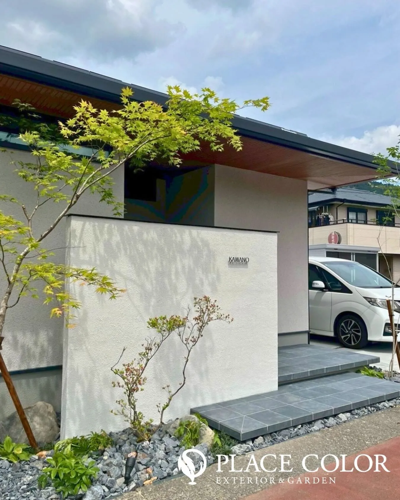 グレーのタイル階段がアプローチをすっきりと整え、足元には石と...