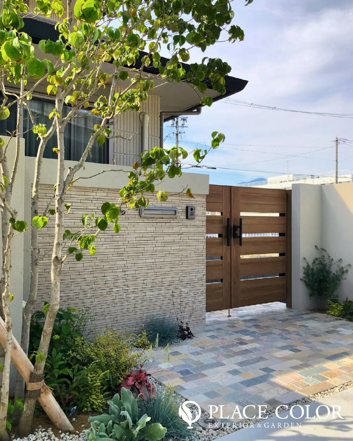 横スリットの木調ゲートと明るい石調の門柱が調和し、やわらかな...